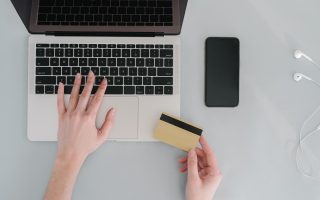 Hænder på en bærbar computer med betalingskort og telefon ved siden af