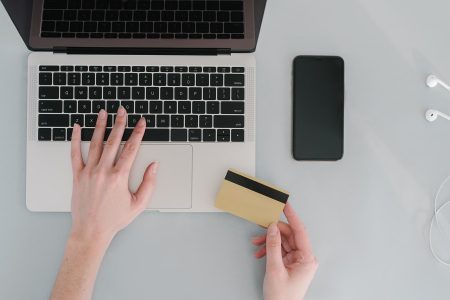 Hænder på en bærbar computer med betalingskort og telefon ved siden af